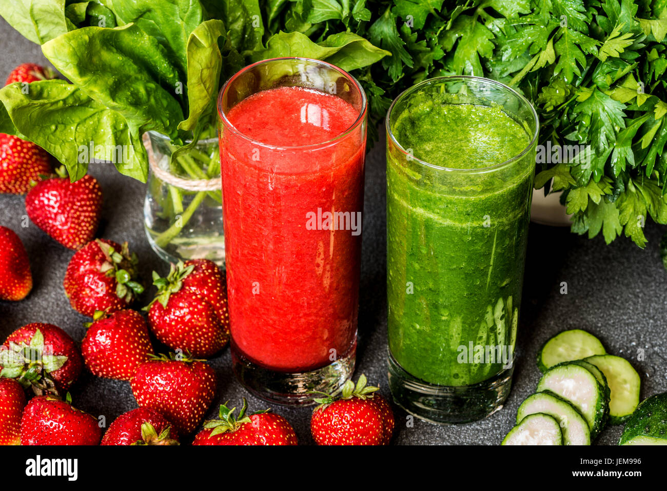 Frullato di fragole e il frullato verde in due bicchieri con ingredienti su sfondo grigio. Detox drink salutari. Foto Stock