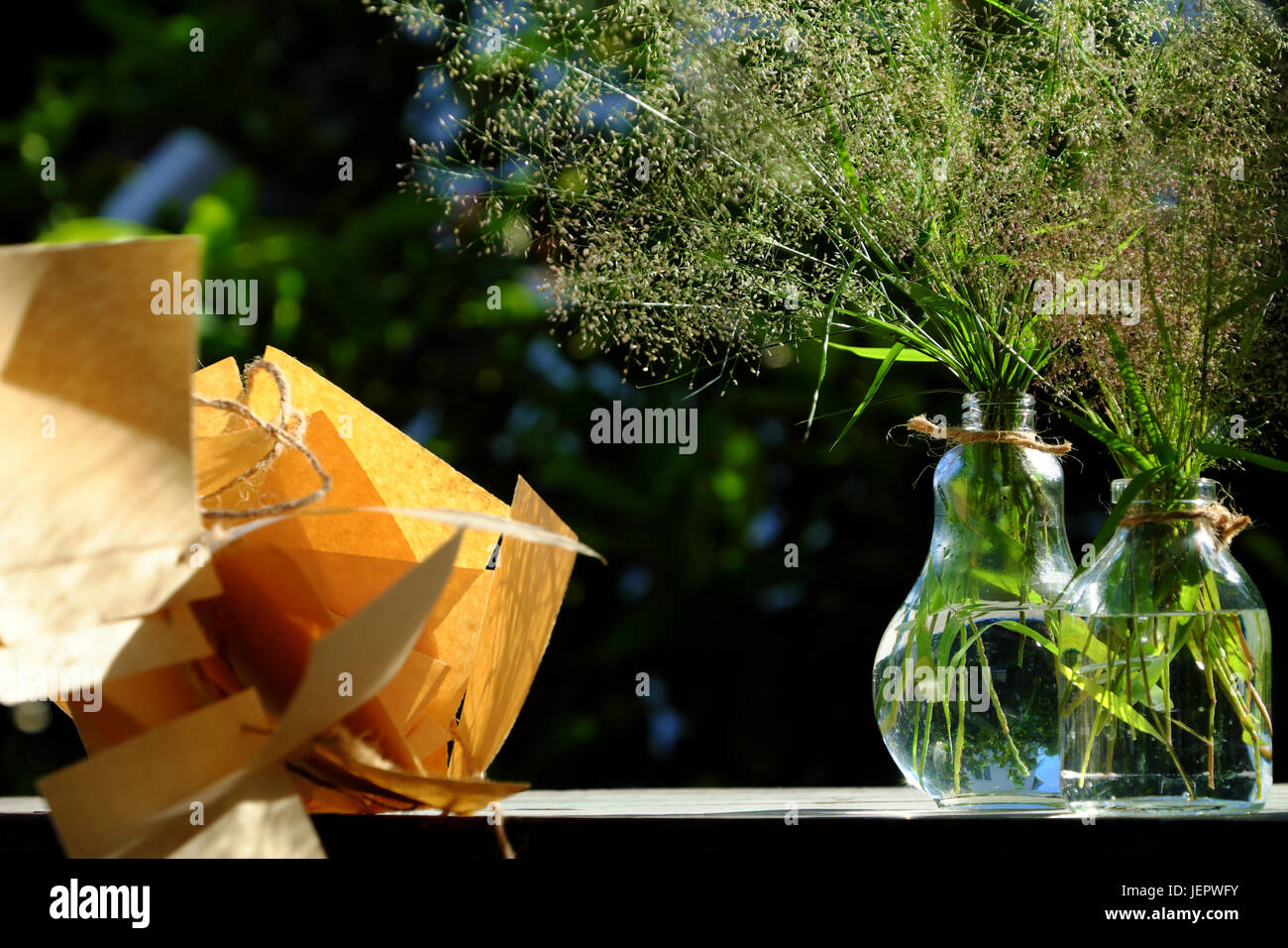 Erba di fiori in vaso di vetro con nota della carta nel vento soffiare al sole di sera fanno di sentimento e di calma, wild minuscoli fiori sul verde sfondo naturale in giardino Foto Stock