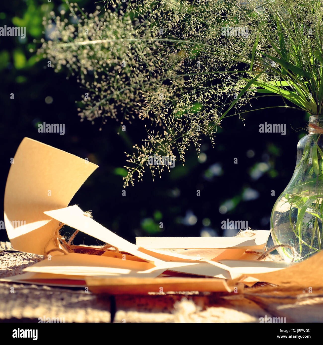 Erba di fiori in vaso di vetro con nota della carta nel vento soffiare al sole di sera fanno di sentimento e di calma, wild minuscoli fiori sul verde sfondo naturale in giardino Foto Stock