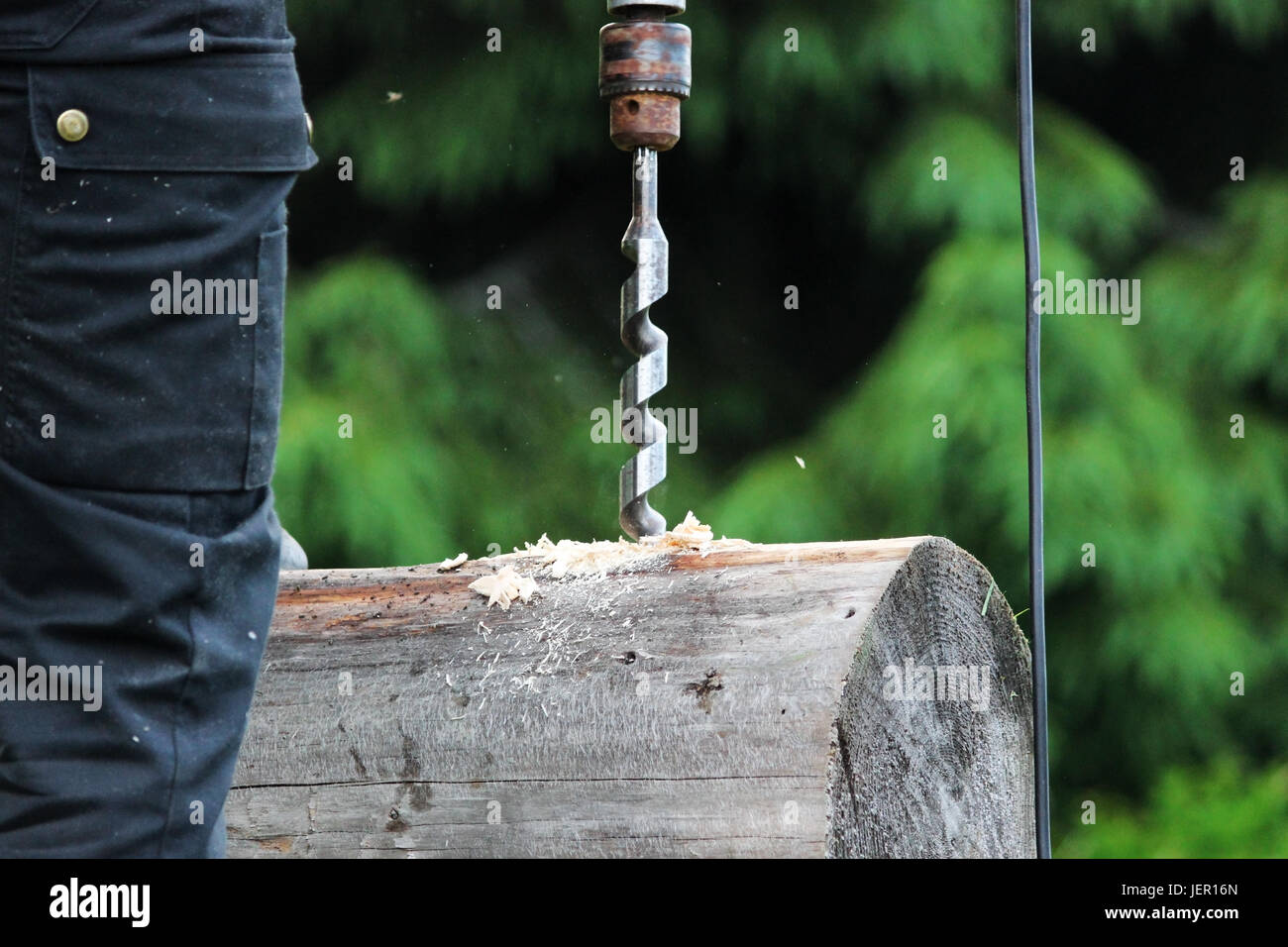 Il lavoratore raccoglie il telaio e le esercitazioni di un foro in un registro per il grano utilizzando un trapano quando la costruzione di una casa in legno Foto Stock