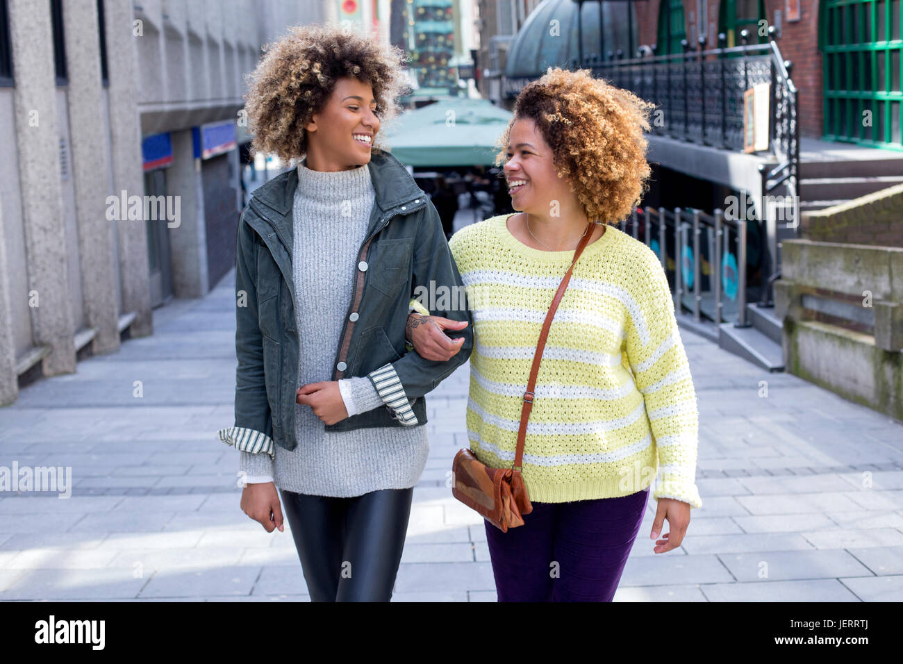 Gli amici passeggiando a braccetto attraverso la città. Essi stanno cercando in ogni altro e ridere. Foto Stock
