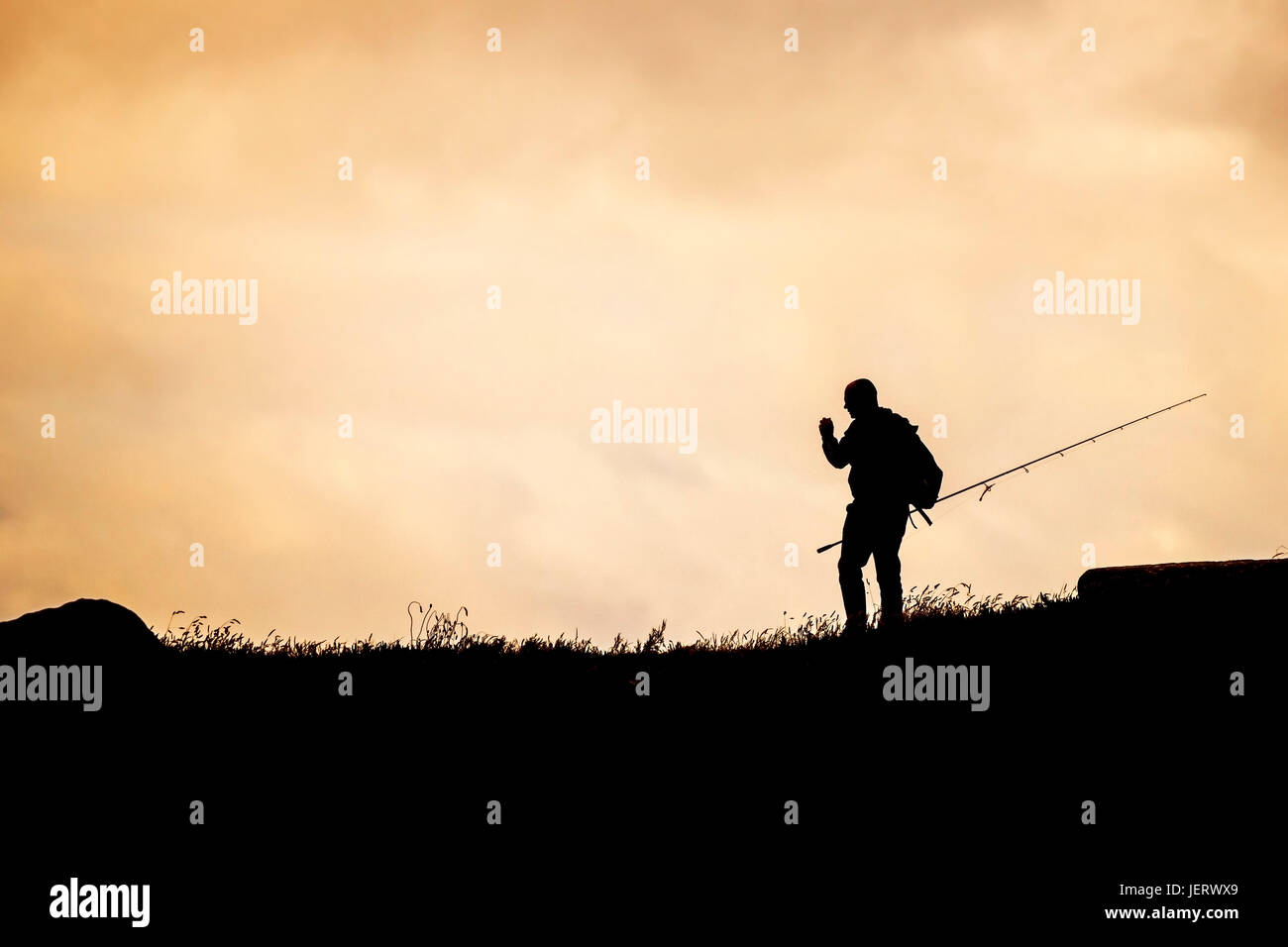 La silhouette di un pescatore in cerca di un posto per il pesce da sul promontorio in Newquay, Cornwall. Foto Stock