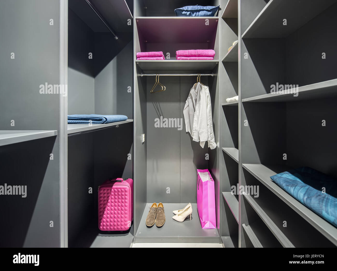 Accesa GRIGIA cabina armadio con molte mensole. Ci sono scarpe, camicie, appendiabiti, asciugamani, cuscino blu, rosa sacchetti. In ambienti chiusi. Orizzontale. Foto Stock