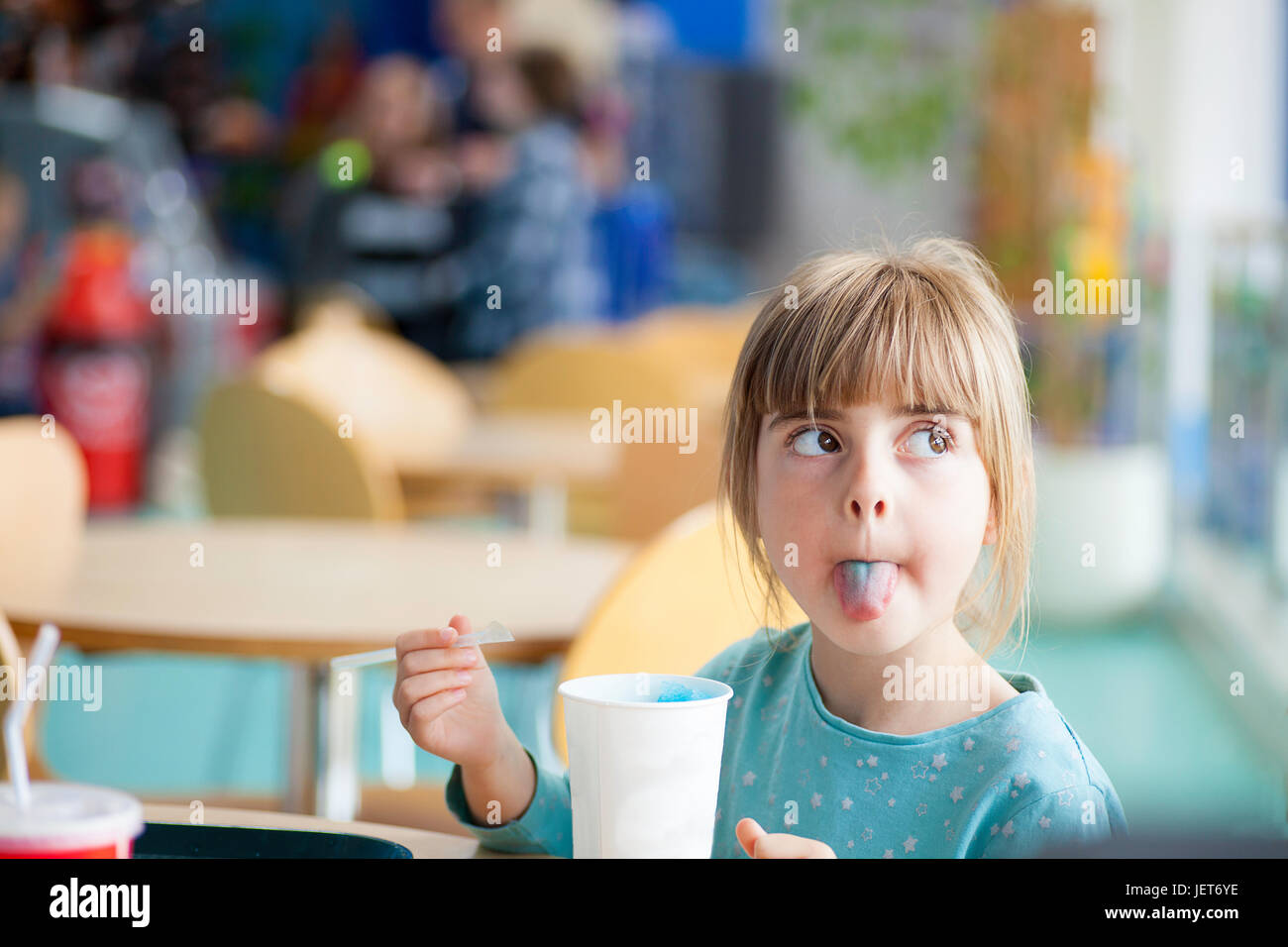 Carina ragazza bionda grippaggio o di dover praticare la lingua di fuori con blue granita in illuminate di luce naturale bar o ristorante Foto Stock