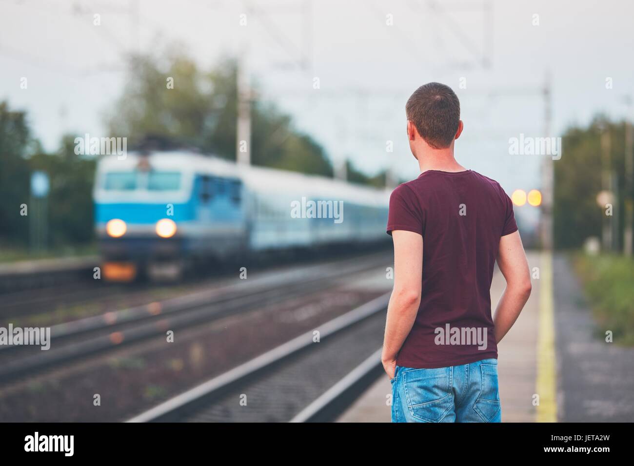 Il viaggio in treno. Giovane uomo in attesa sulla piattaforma oft stazione ferroviaria. Foto Stock