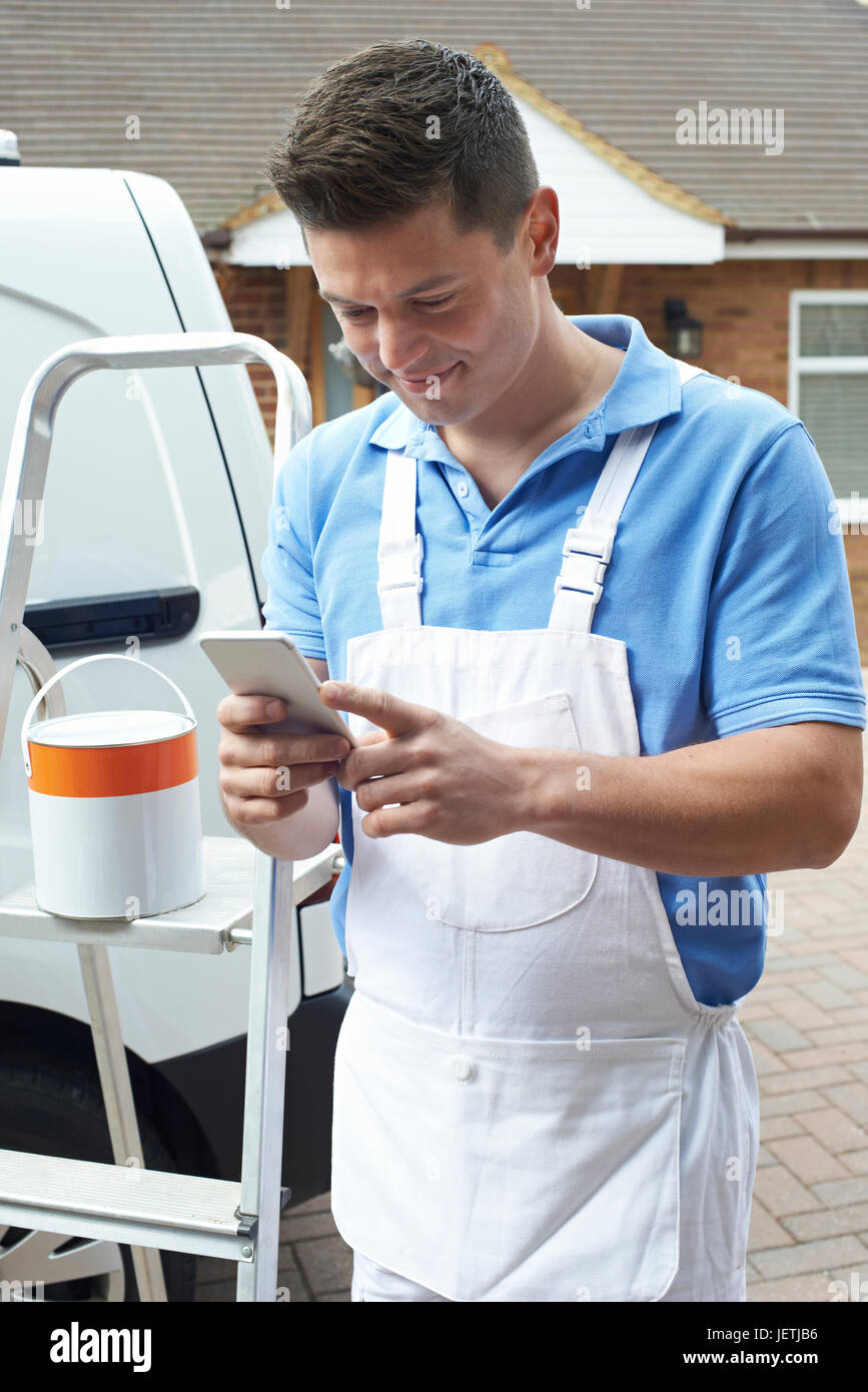 Arredatore tramite telefono cellulare in piedi fuori casa domestico Foto Stock