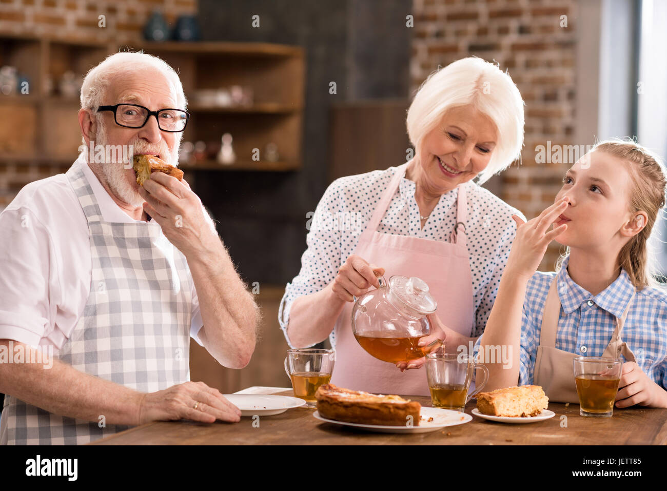 Nonni e una ragazza bere il tè con torta insieme a casa Foto Stock