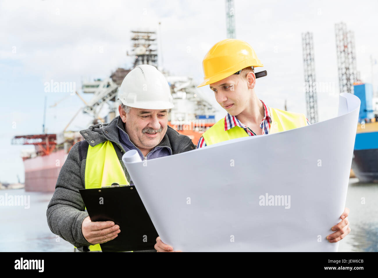 Ingegnere navale discute i documenti con uno studente. Lavoratore esperto bianco che indossa il casco di sicurezza spiega i problemi tecnici per un manuale labore Foto Stock