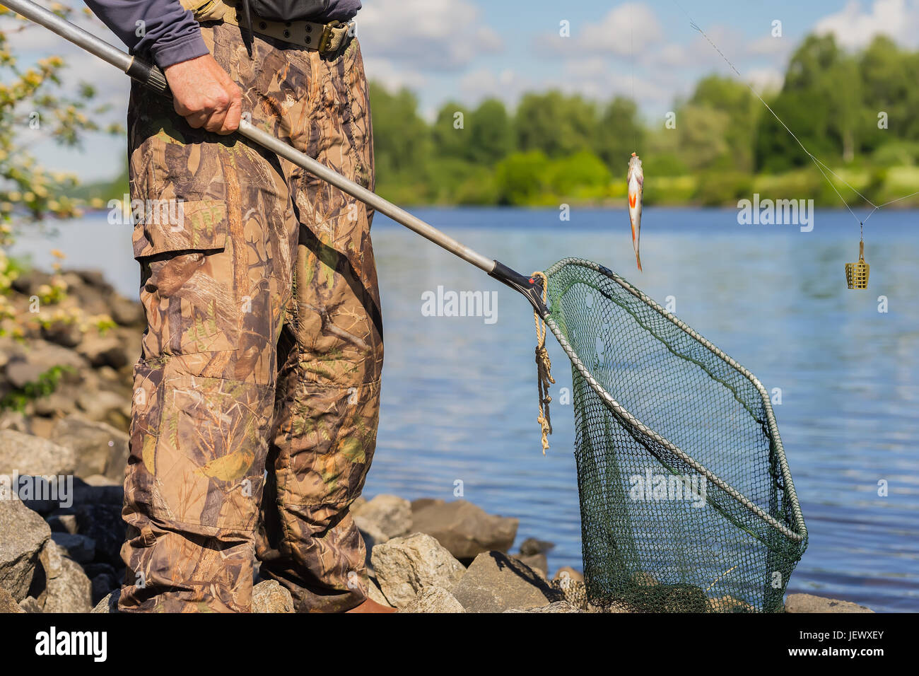 Un irriconoscibile di mezza età pescatore con un vecchio net con un foro e un piccolo pesce appena pescato sulla linea. Concetto di attivo uno stile di vita sano a qualsiasi età Foto Stock