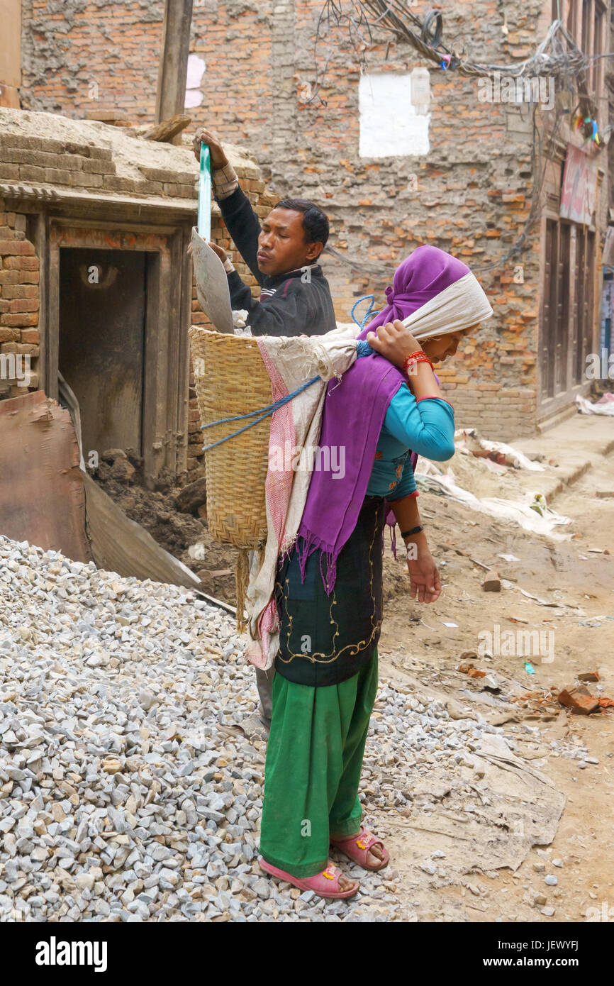 Uomo di ghiaia di caricamento in un cesto portato da una donna, Bhaktapur, Nepal. Foto Stock