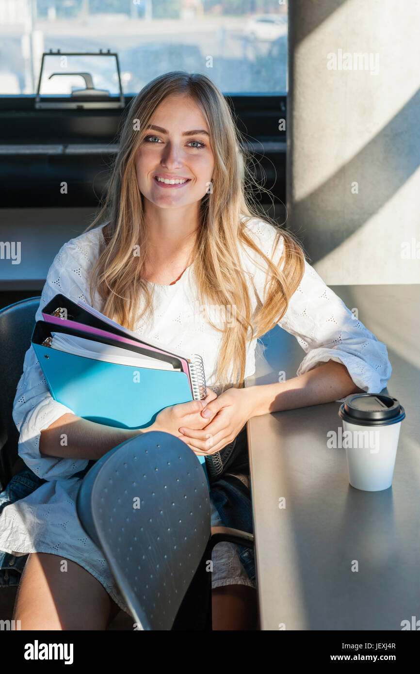 Sorridente donna giovane studente con libri e leganti che studiano in un area di studio di università o college campus Foto Stock