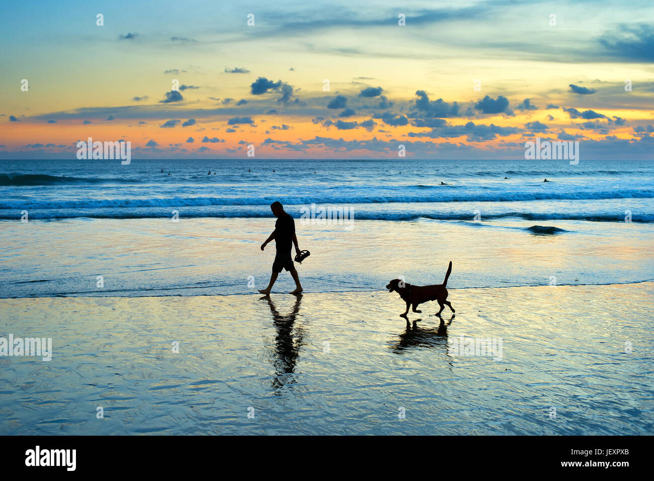 Silhouette di uomo e cane a camminare su una spiaggia al tramonto. Isola di Bali, Indonesia Foto Stock