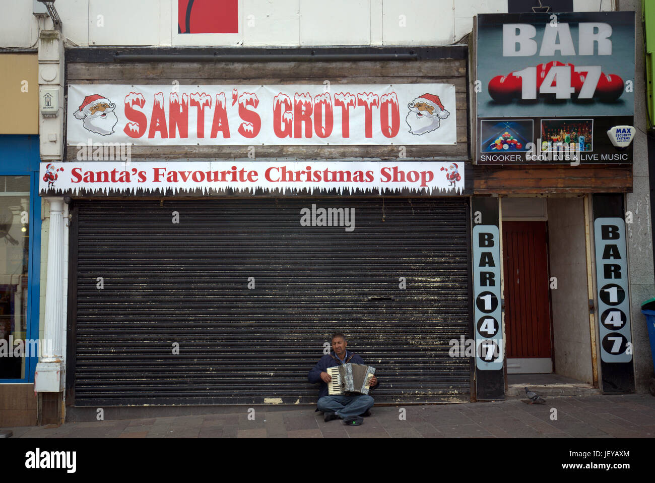 Mendicare senzatetto disoccupati uomo suonare la fisarmonica di Natale babbi natale sfondo grotta shop macrocosmo della moderna Gran Bretagna Foto Stock