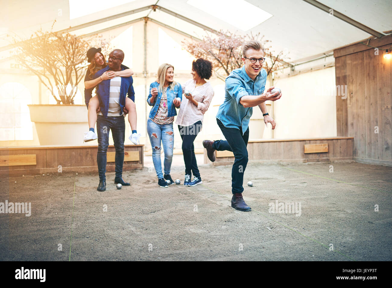 Uomo eccitato di gettare una sfera di gioco bocce mentre in bianco e nero amici comunicante. Foto Stock