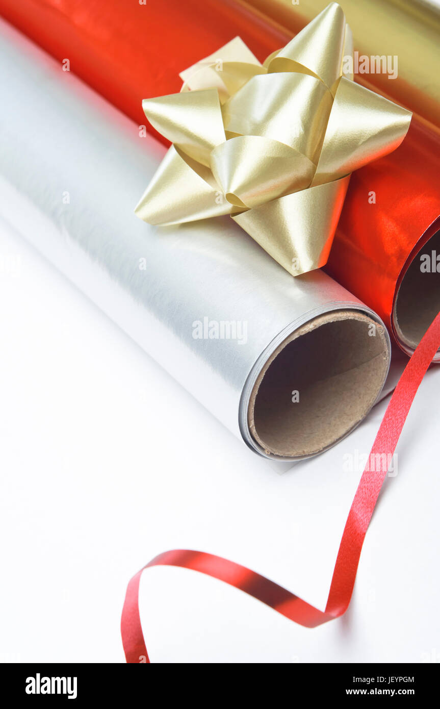 Close up, colpo angolato di confezione regalo rotoli di carta, Rosetta e nastro su una superficie bianca. Foto Stock