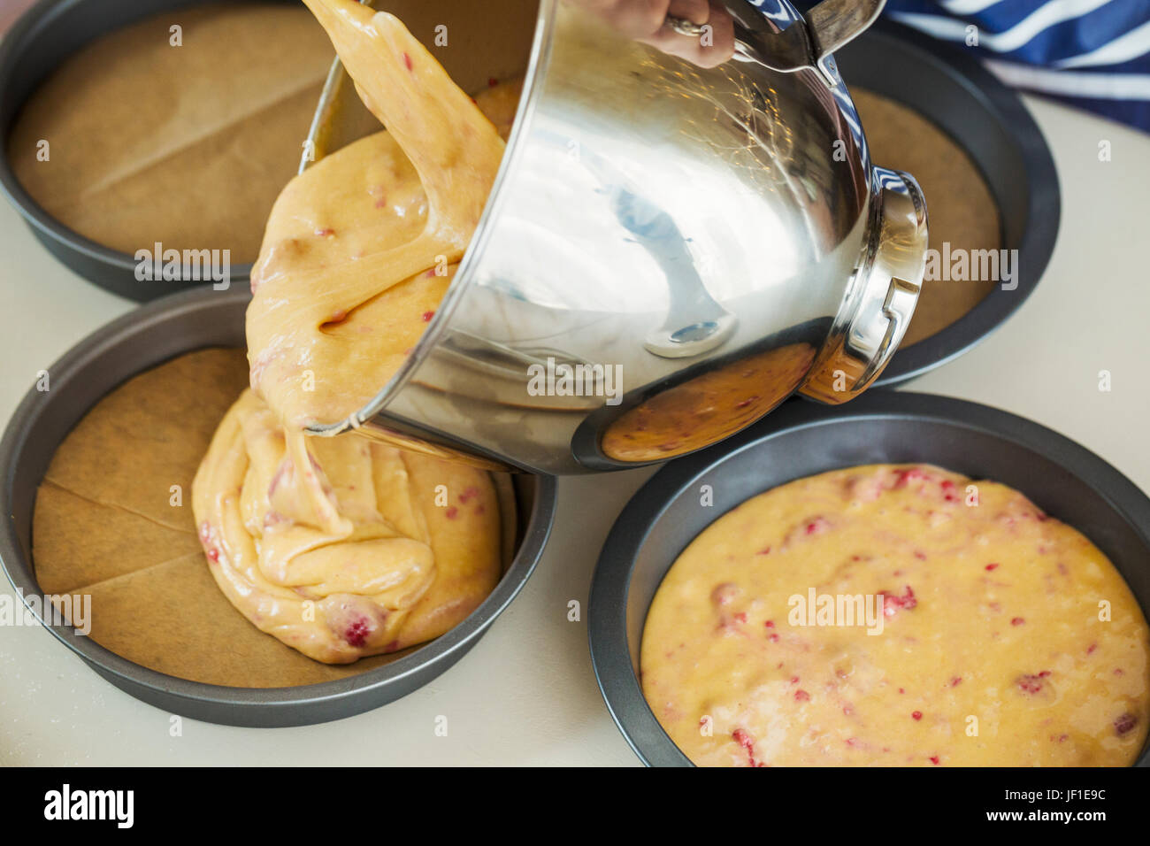 Chiudere fino ad alto angolo di visione dell'impasto che viene versato di metallo recipiente di miscelazione nel round di teglie. Foto Stock