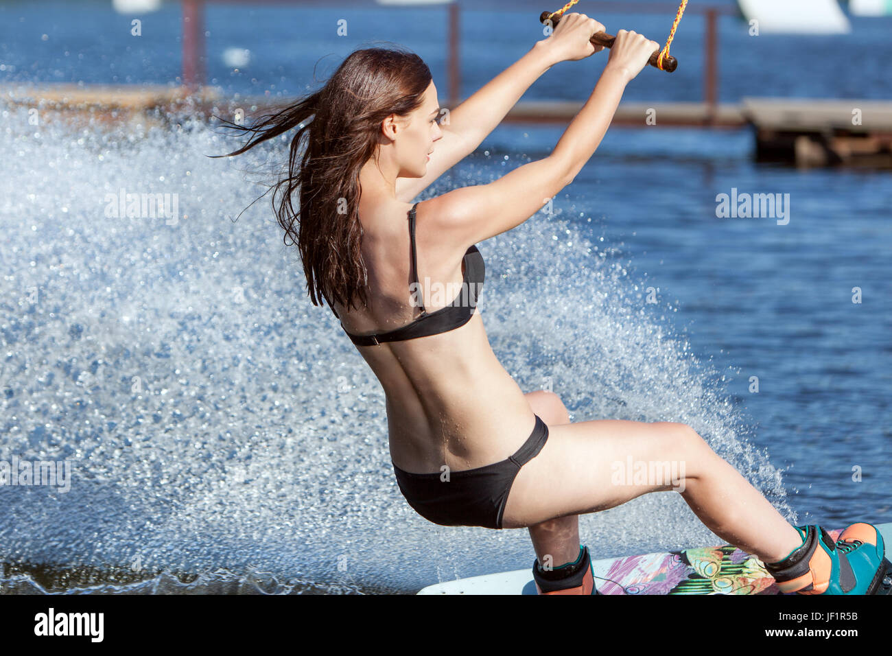 Donna in costume da bagno pattini sul lago sul wakeboard. Foto Stock