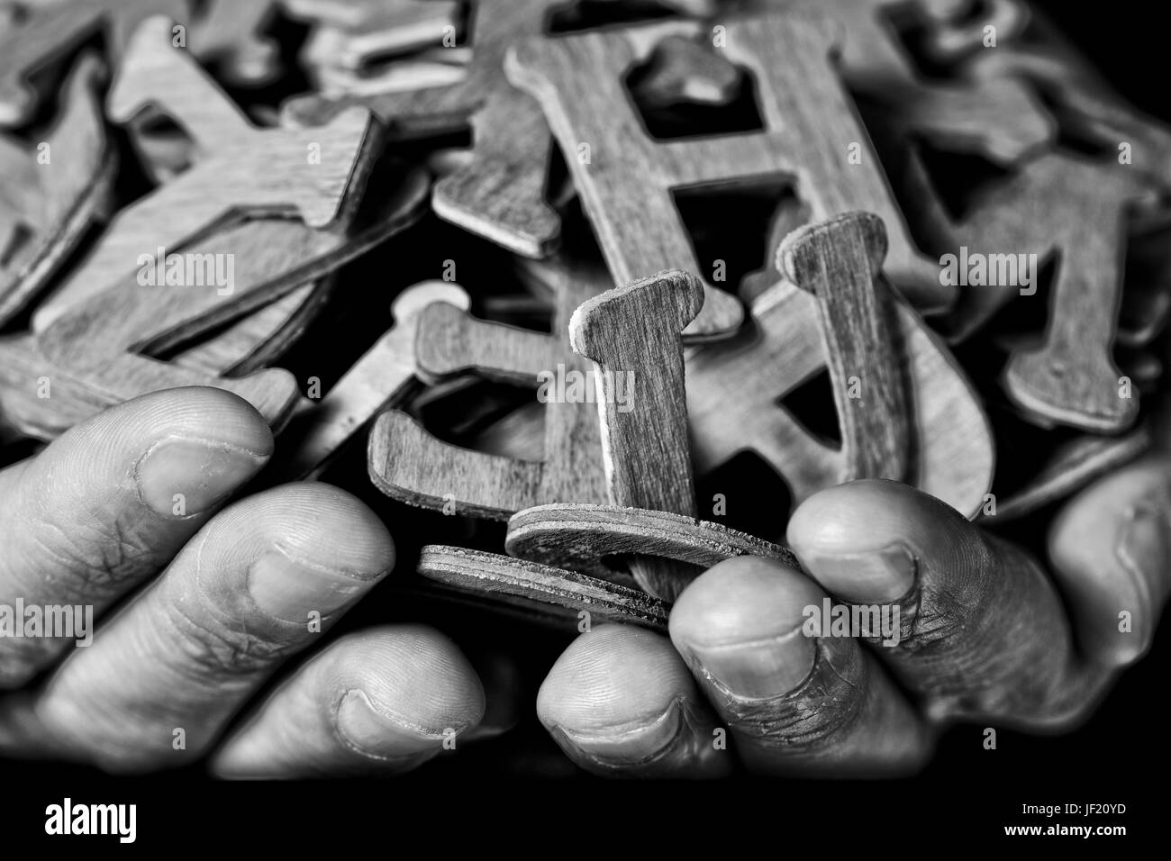 Primo piano delle mani di un giovane uomo caucasico tenendo un pugno di diverse lettere di legno, in bianco e nero Foto Stock