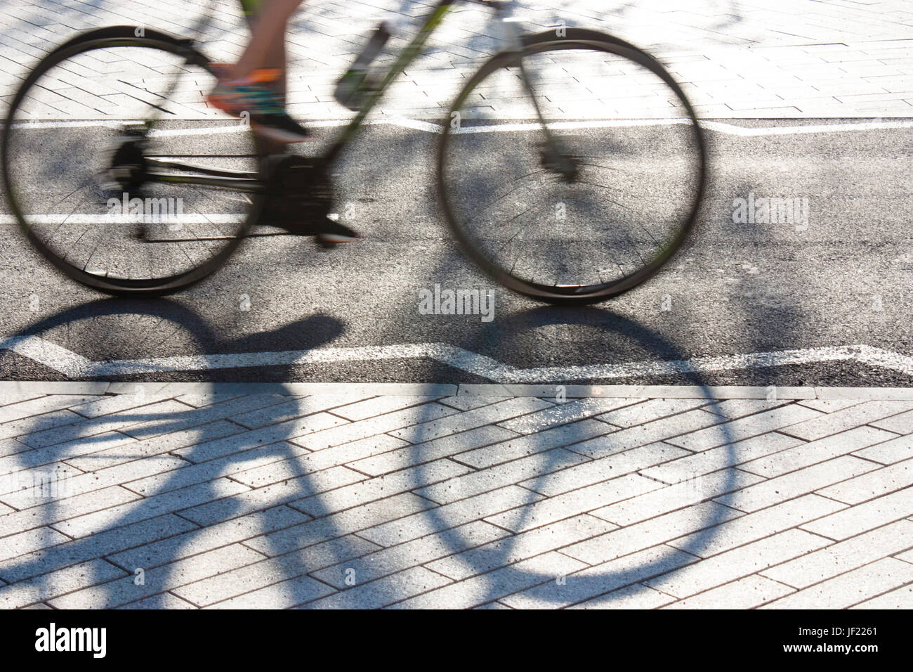 Sfocata ciclista silhouette e ombra su un asfalto pista ciclabile accanto al marciapiede pedonale marciapiede Foto Stock