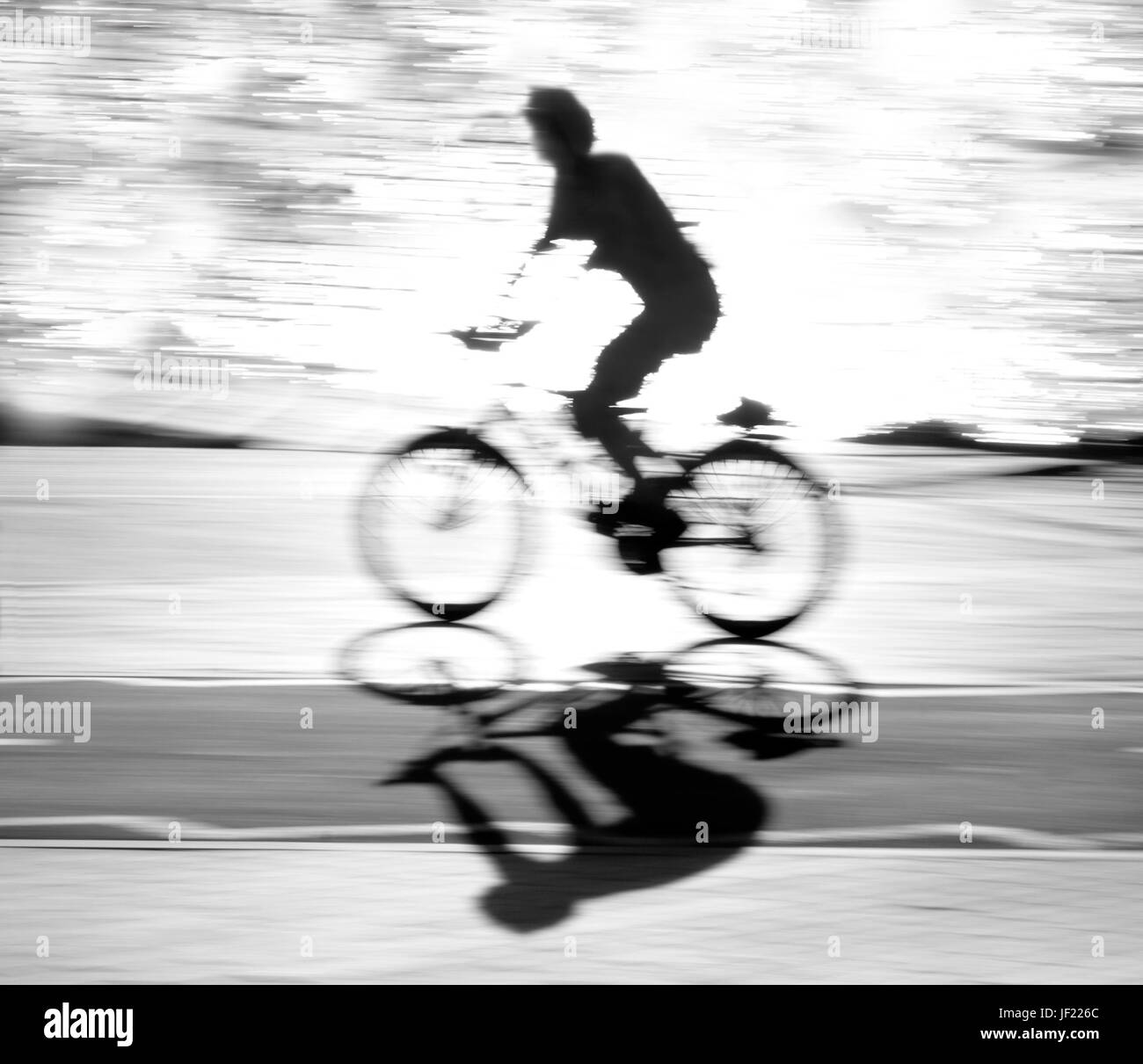 Ciclista sfocati silhouette e ombra su di una pista ciclabile lungo il fiume con acqua la riflessione in bianco e nero a contrasto elevato Foto Stock