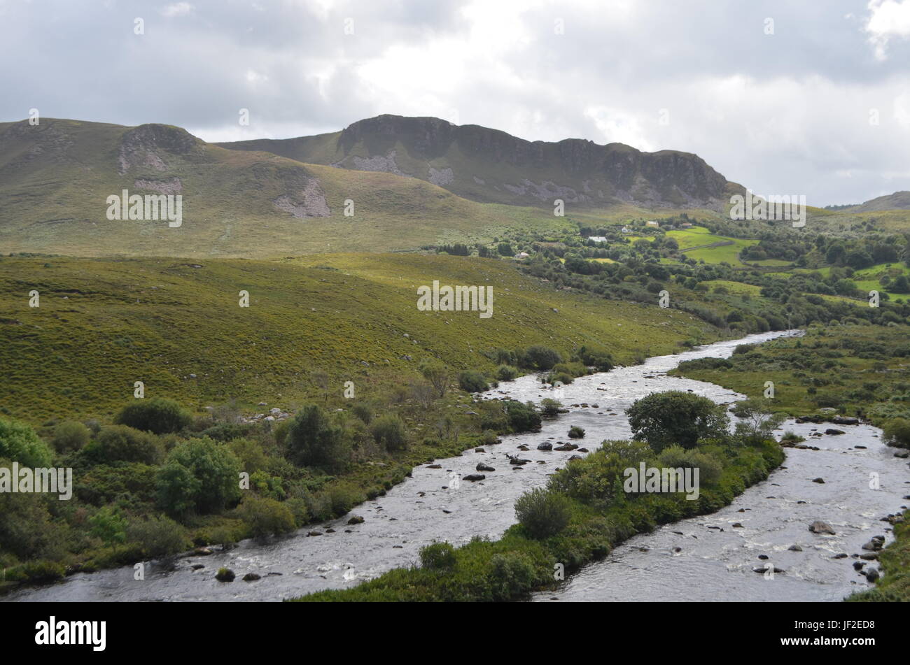 Piccolo fiume che scorre nella verde vegetazione e paesaggio di montagna in una strada nazionale in Irlanda Foto Stock