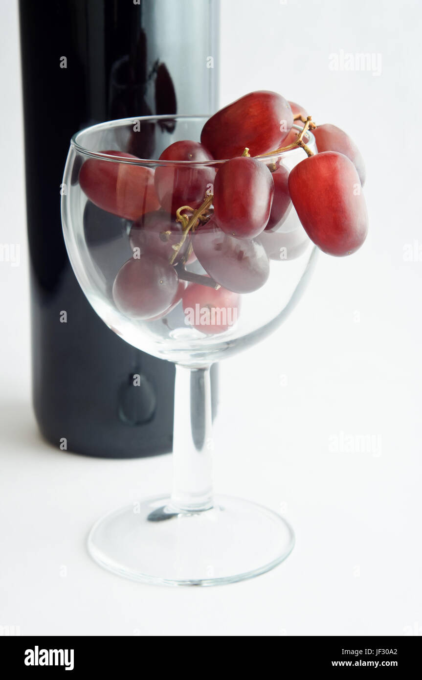 Un vino di vetro riempita con uve rosse davanti ad una bottiglia di vino rosso. Orientamento verticale. Foto Stock