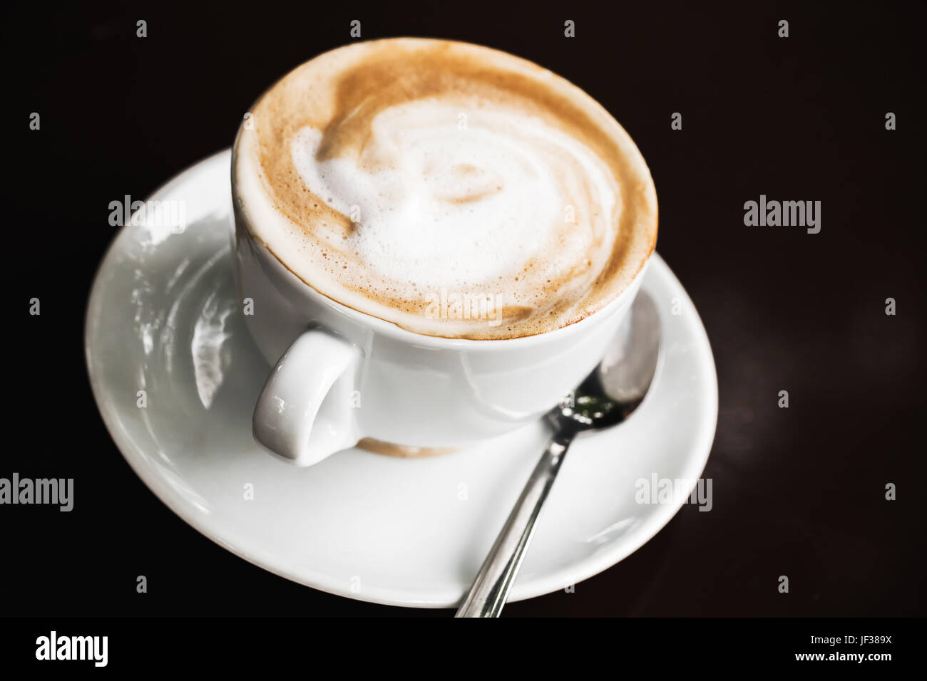 Tazza di cappuccino. White la tazza di caffè con la schiuma di latte sul nero sfondo tabella, il fuoco selettivo Foto Stock