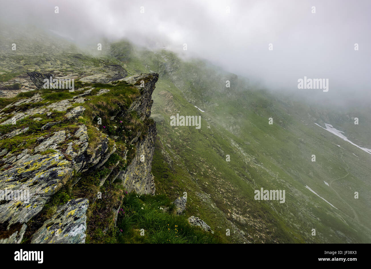 Bordo del ripido pendio sulla collina rocciosa nella nebbia meteo. lo scenario spettacolare in montagna Foto Stock