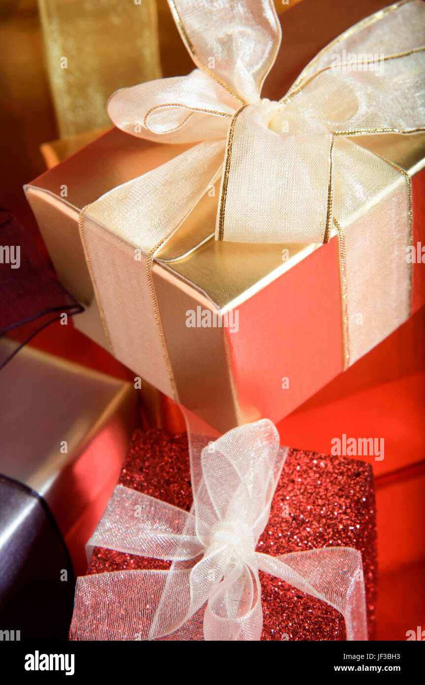 Un mucchio di regali di Natale, in brillante e vivace imballaggio, legato in ribbosns con archi su un rosso superficie riflettente. Orientamento verticale. Foto Stock