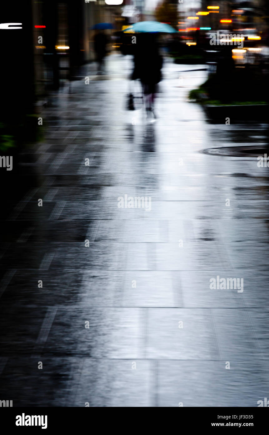 Verticale di soft focus immagine di una donna che porta un ombrello blu sotto la pioggia a piedi dalla fotocamera. Foto Stock