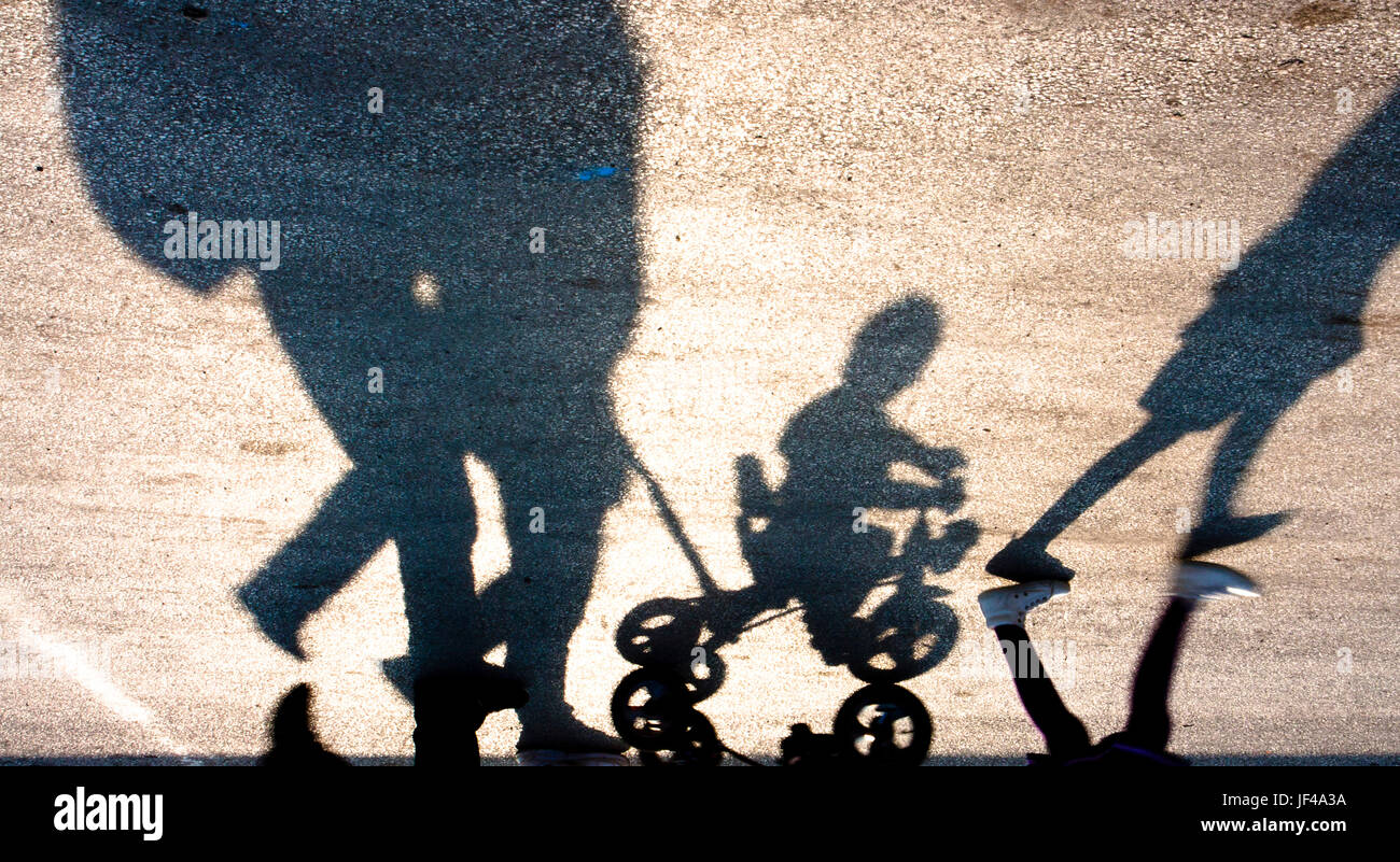 Sagome sfocate e le ombre di una famiglia a piedi con due bambini, uno su un piccolo tre ruote di bicicletta, capovolto Foto Stock