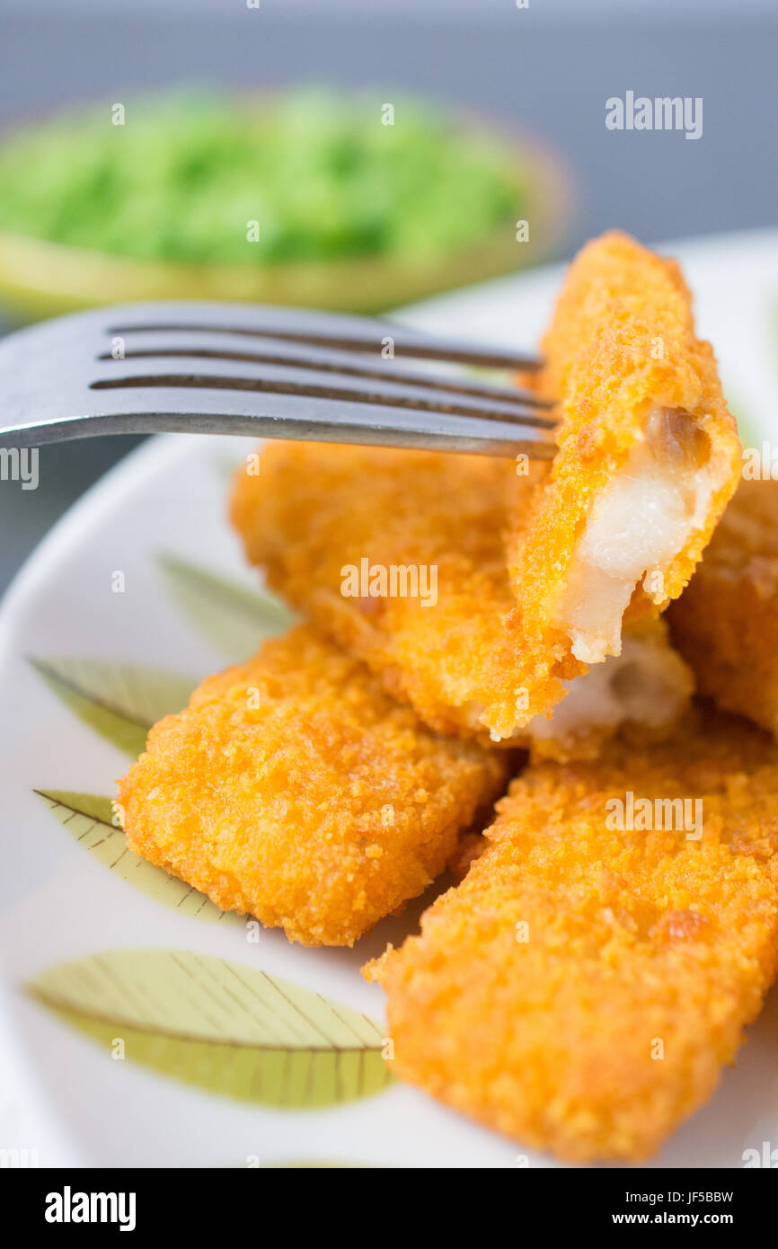 Impanati e cotto bastoncini di pesce, le dita su una piastra con una ciotola di piselli e una fettina di limone Foto Stock