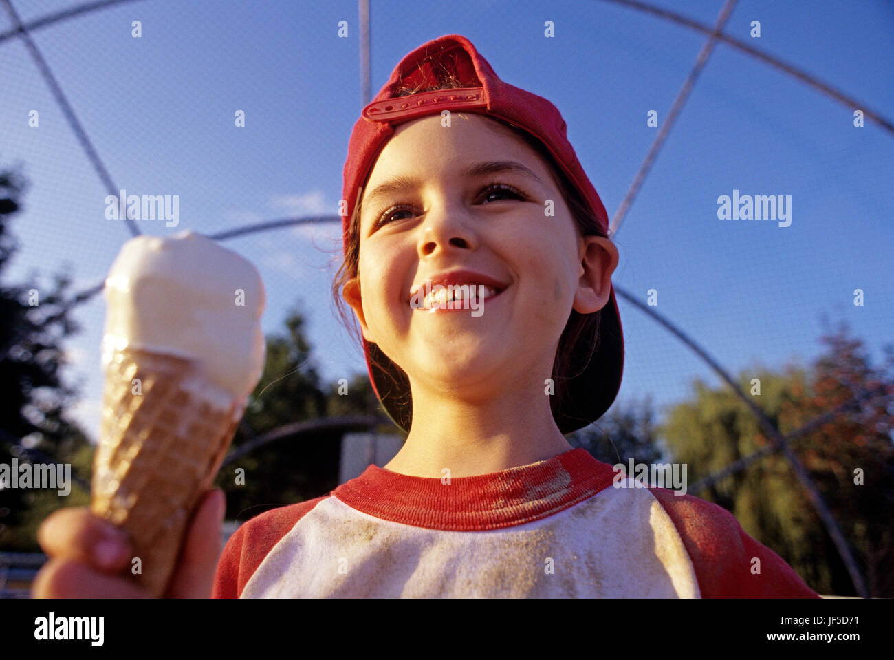 Ragazza giovane (7 anni), Little League Baseball player, a mangiare il gelato dopo il gioco, la luce del tramonto, ritratto USA Foto Stock