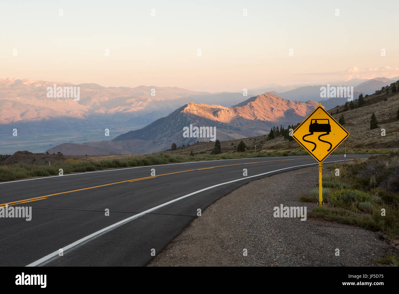 Un segnale di avvertimento per una curva Winding Road passando attraverso le montagne in El Dorado National Forest. Foto Stock