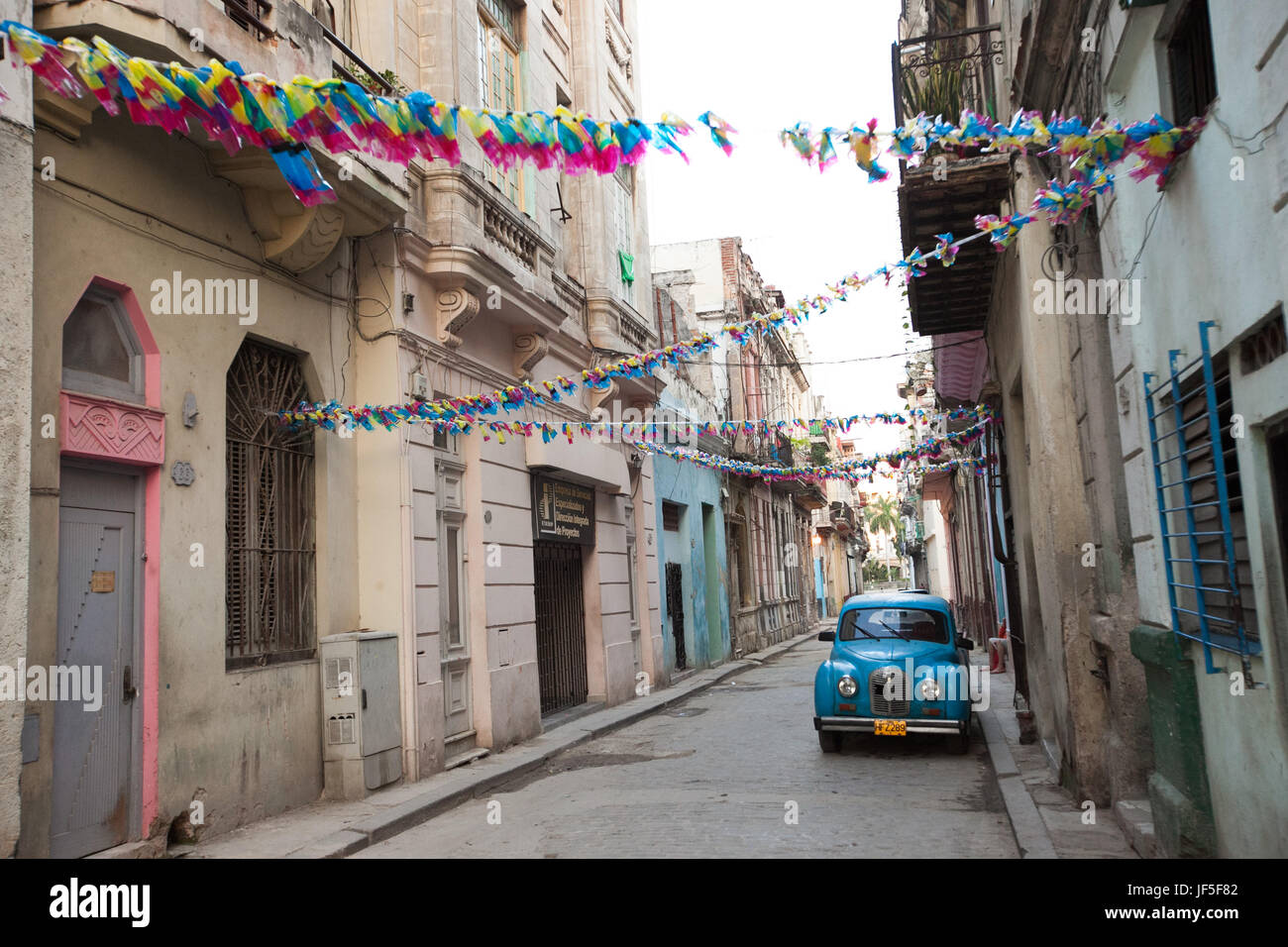 Al di sopra di una classica vettura americana, decorazioni colorate appendere da edifici su una stradina nel centro di Havana. Foto Stock