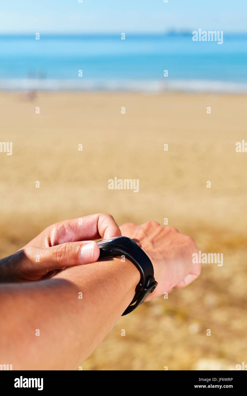 Primo piano di una giovane atleta sincronizzando il suo smartwatch, con il mare in sottofondo e un grande spazio vuoto sopra di lui Foto Stock