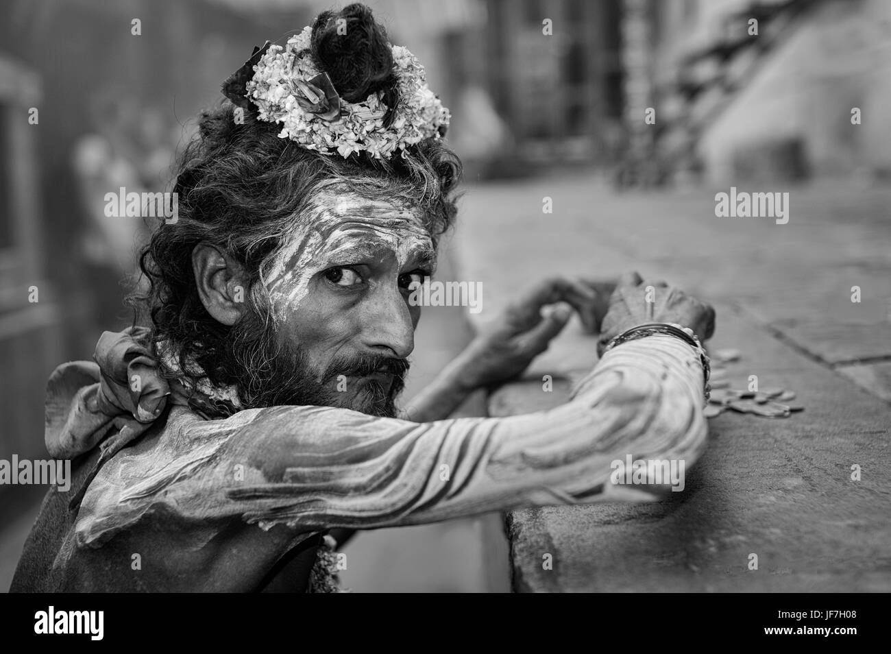 Sadhu, Indù uomo religioso, con la faccia di vernice e fiori, conta i suoi magri incassi da accattonaggio in Varanasi, Uttar Pradesh, India. Foto Stock