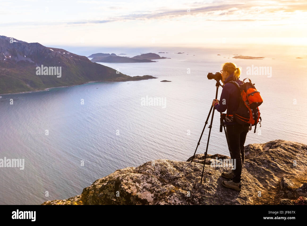 Donna fotografo di prendere foto di un bellissimo fiordo in Norvegia al golden ora con fotocamera DSLR e treppiedi Foto Stock