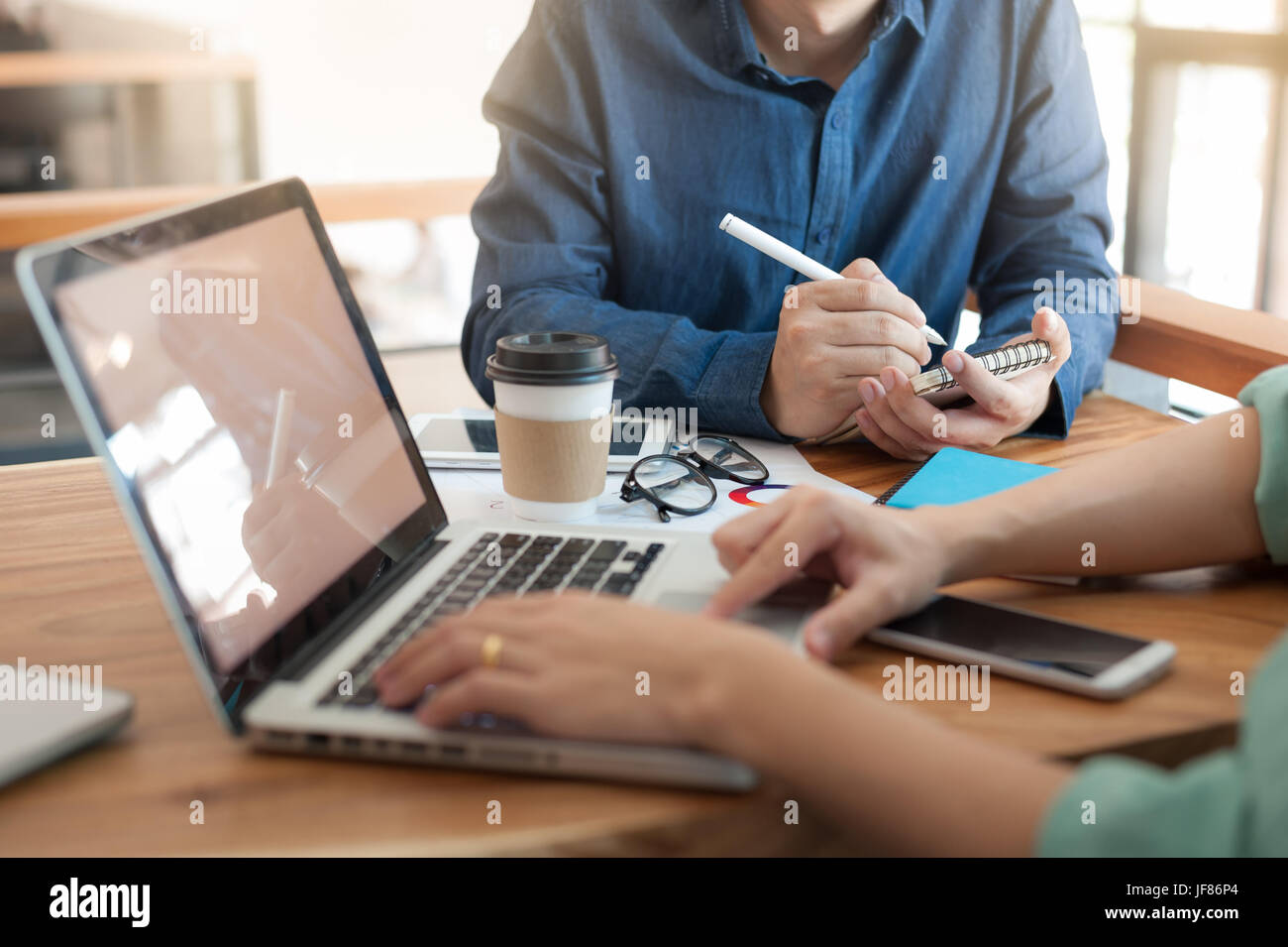 Giovani hipster lavoratore iscritto sul piccolo notebook mentre sale riunioni con i colleghi di Coworking Space. freelancer il lavoro di squadra e il concetto di brainstorming Foto Stock