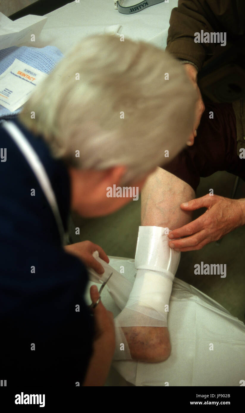 Distretto infermiere su una home visita medicazione un persone ulcere della gamba Foto Stock