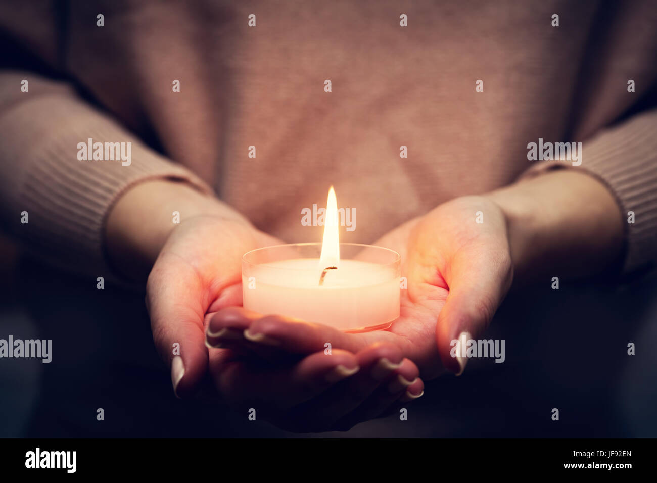 La luce di una candela incandescente nella donna con le mani in mano. La preghiera, la fede, il concetto di religione. Foto Stock