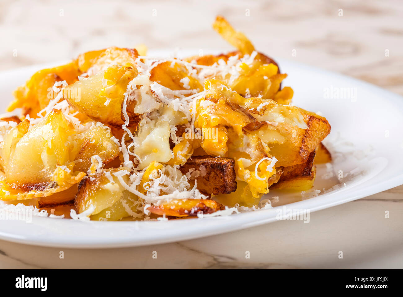 Patate fritte con uova strapazzate e parmigiano sulla piastra bianca Foto Stock