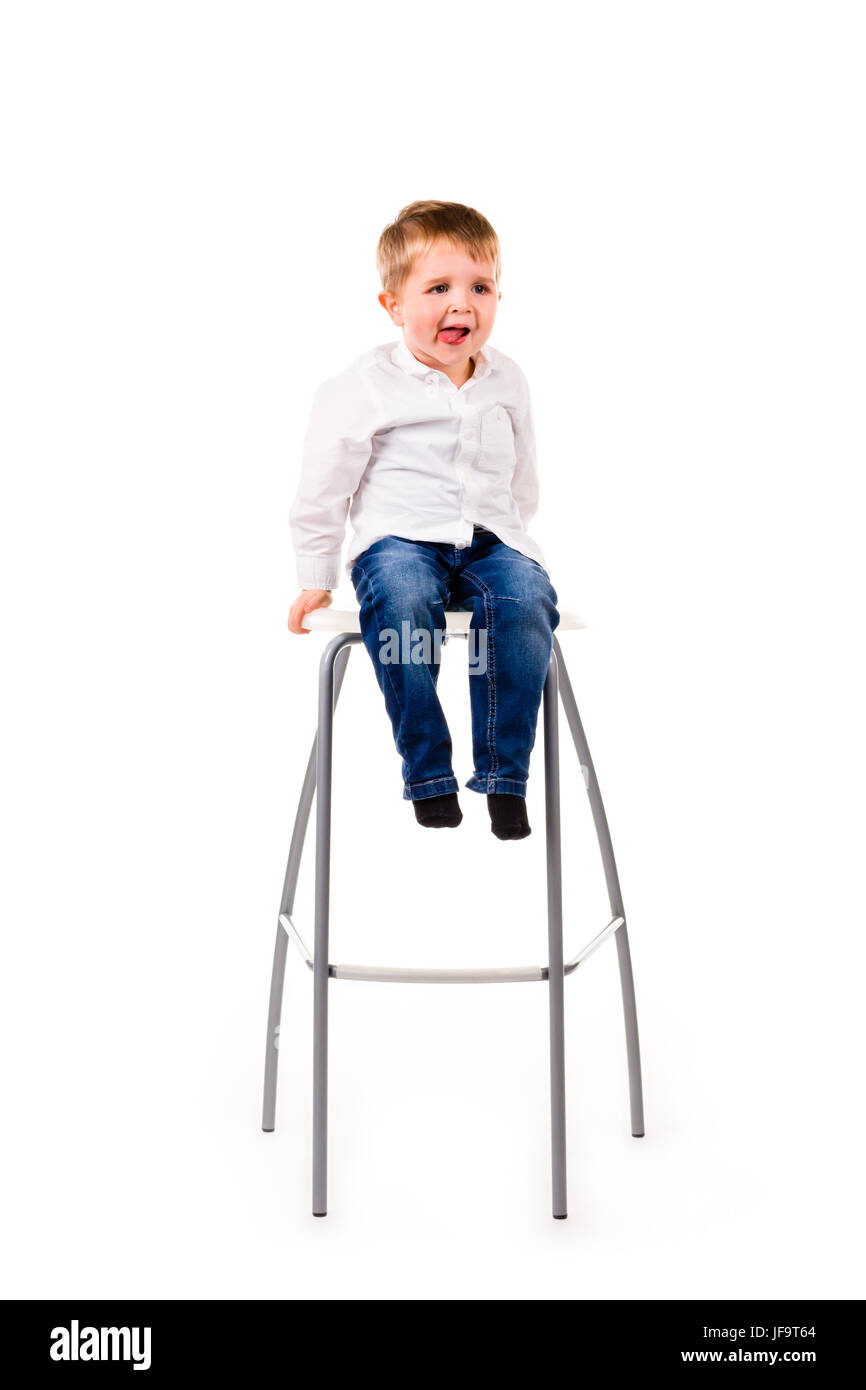 Piccolo Ragazzo seduto su uno sgabello fuori la sua lingua. Isolato su uno sfondo bianco Foto Stock