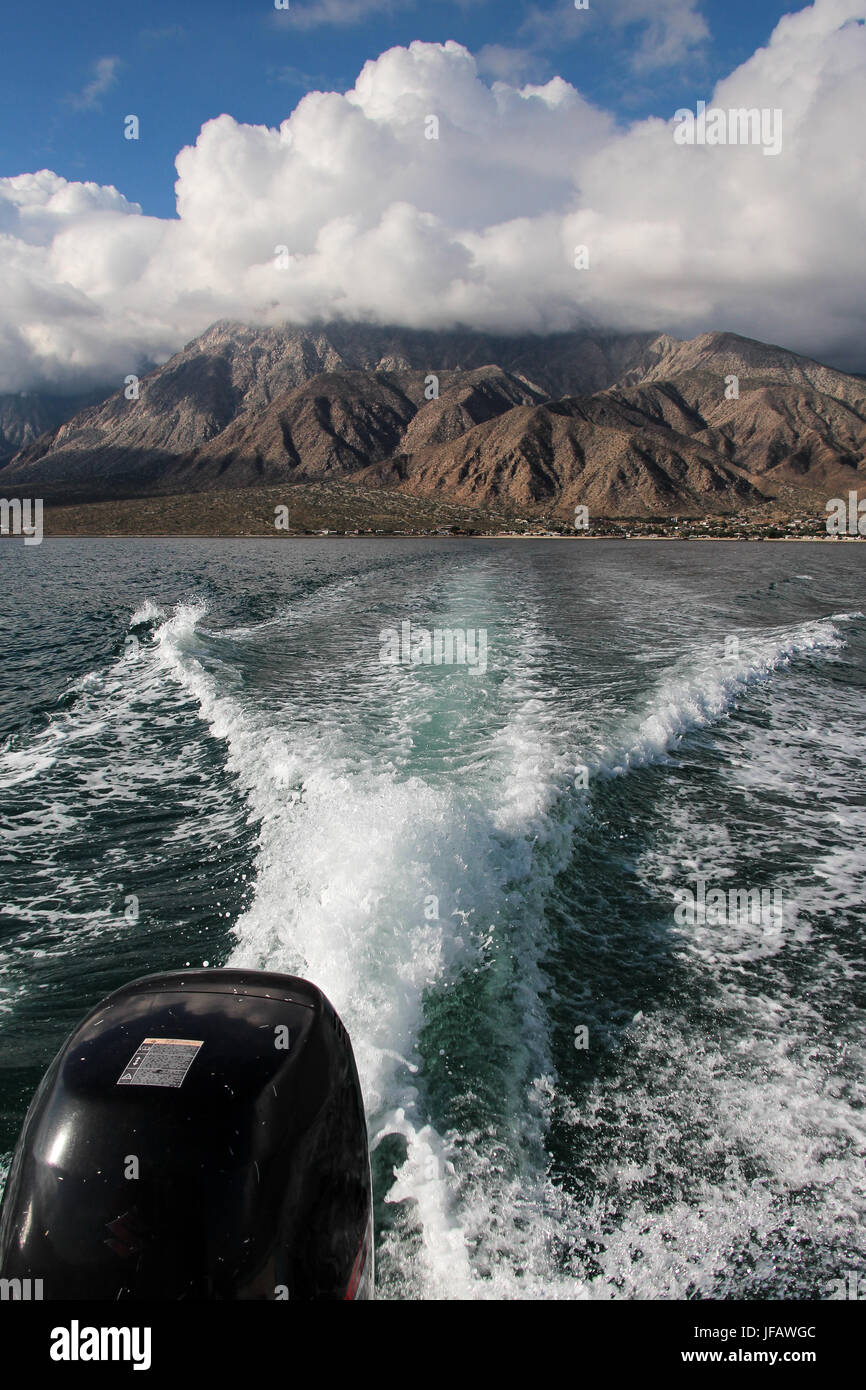 Zoom indietro di Bahia de los Angeles in una barca fuoribordo, sulla scia rendendo un pattern in acqua; cloud-coperta Sierra de San Borja, la baia dietro di noi. Foto Stock
