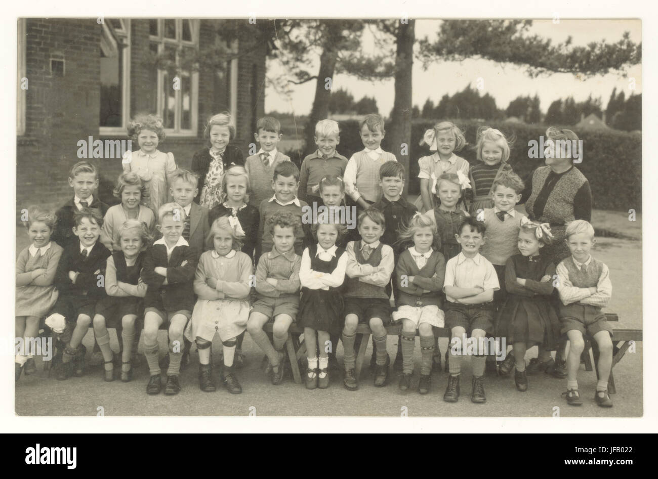 Cartolina raffigurante una classe di bambini delle scuole con il loro insegnante al di fuori che pongono in estate uniforme, in prima fila è una ragazza in calibri, probabilmente vittima della poliomielite, circa primi anni cinquanta, U.K. Foto Stock