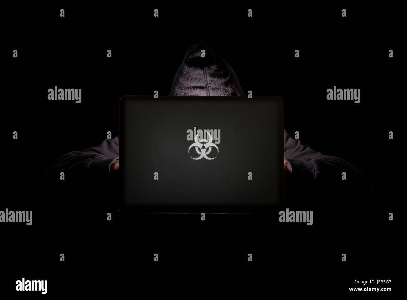 Una persona in una stanza buia che utilizza un laptop con un logo di rischio biologico, phishing su Internet, hacking, minacce alla sicurezza dei dati, violazione dei dati, concetto di sicurezza informatica Foto Stock