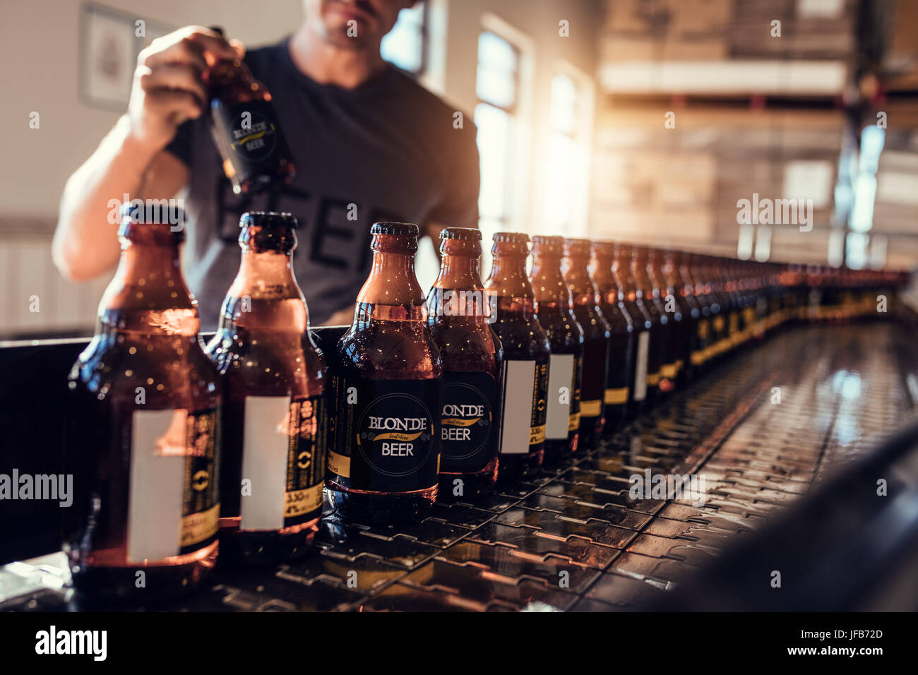 Trasportatore con bottiglie di birra in movimento nella fabbrica di birra. Giovane uomo la supervisione della birra il processo di imbottigliamento e di controllo della qualità a livello di fabbricazione pl Foto Stock