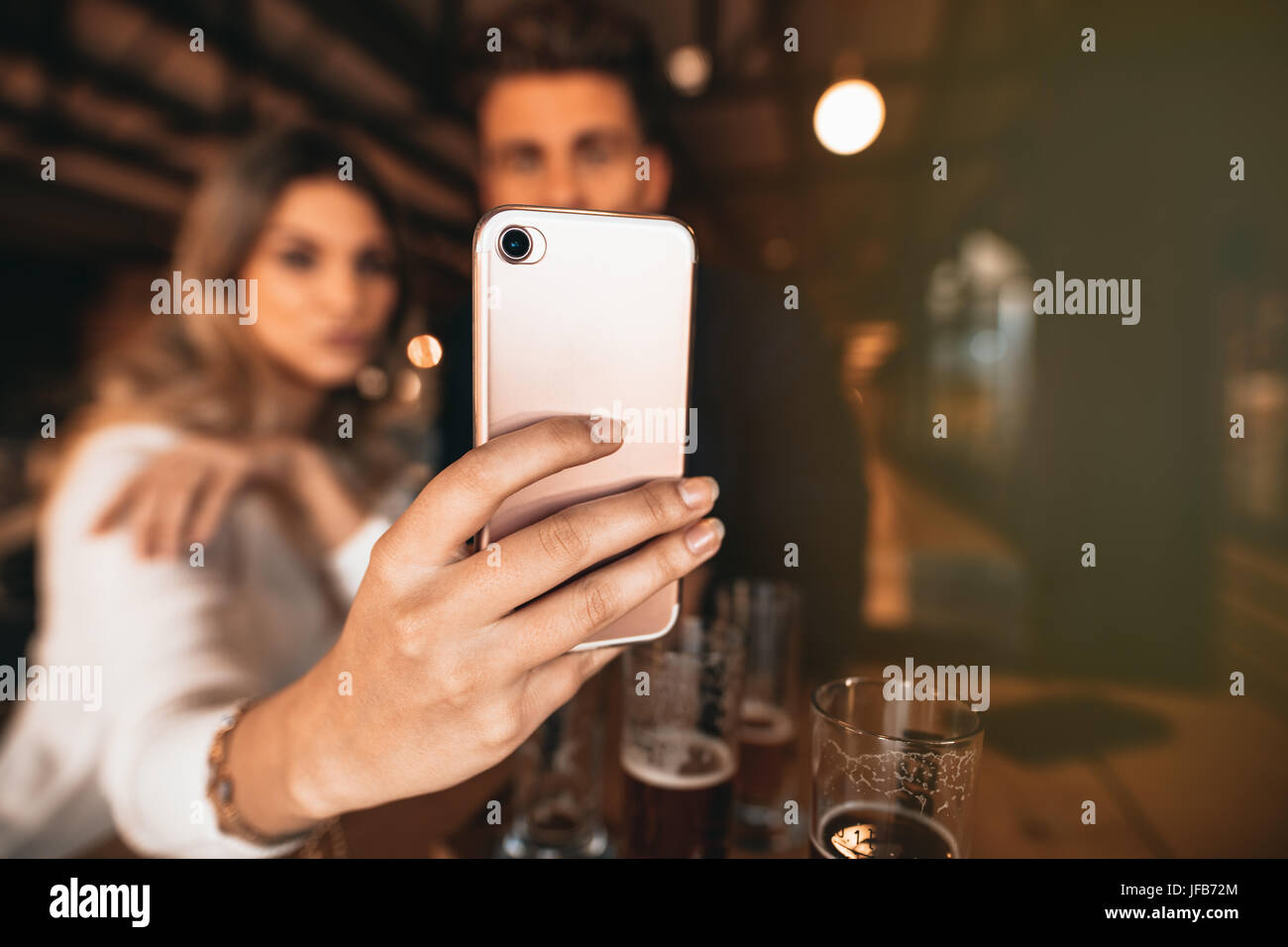 Chiusura del giovane seduto al bar e prendendo un selfie con smart phone. Focus sul telefono cellulare in mano di donna. Foto Stock