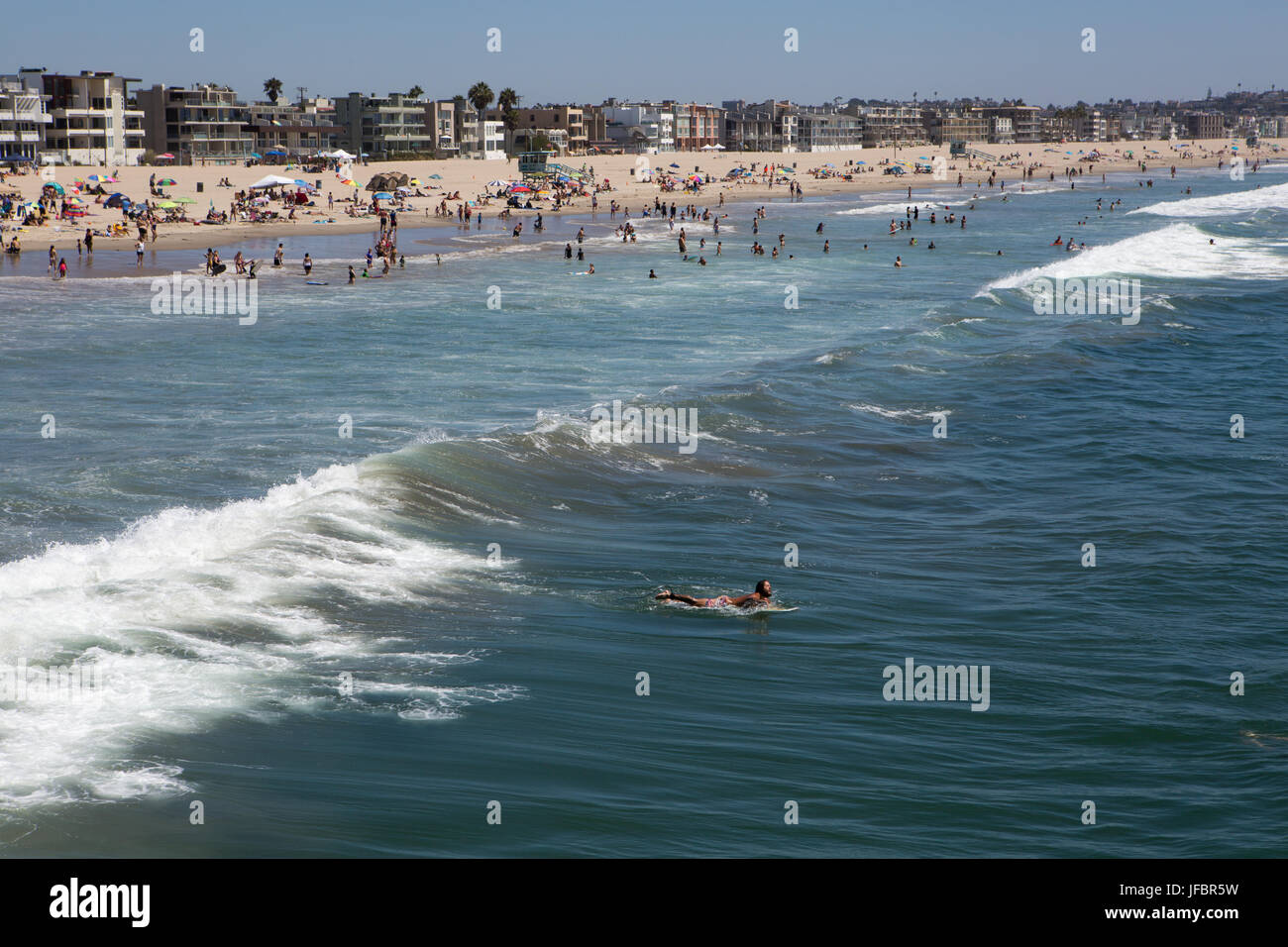Un surfista pagaie lontano dalla folla costante sulla spiaggia di Venezia. Foto Stock