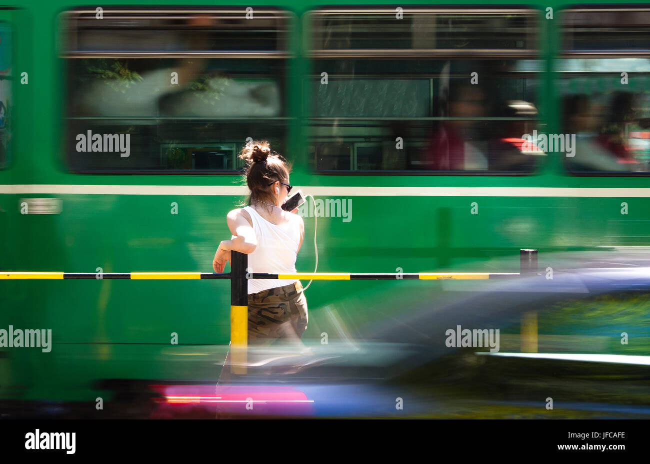 Ragazza adolescente a parlare su un telefono cellulare mentre si è in attesa per il bus in strada trafficata Foto Stock